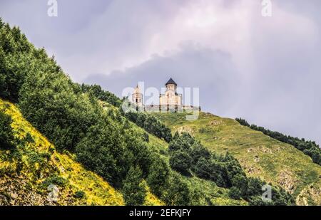 Chiesa della Trinità di Gergeti del XIV secolo vicino al villaggio di Gergeti In Georgia vicino al confine settentrionale con la Russia visto da Villaggio di Stepantsminda o Foto Stock