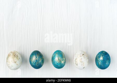 Modello di disegno di Pasqua con uova blu e oro colorate su sfondo bianco di legno con spazio di copia. Design minimalista per banner pasquale in stile moderno. Foto Stock
