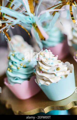 Cupcakes con panna bianca e palline colorate su un oro stand Foto Stock