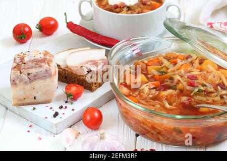 Borsch con pancetta, pane nero su fondo di legno bianco Foto Stock