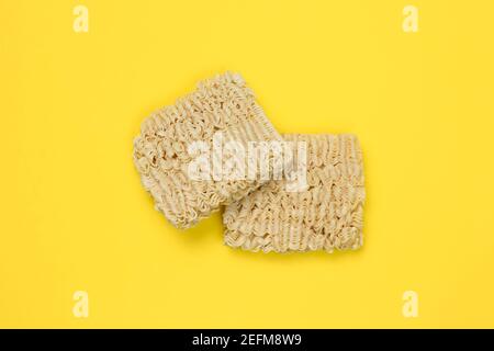 Spaghetti istantanei, ramen, blocchi di noodle secchi su sfondo giallo. Concetto di cibo malsano. Pasta cruda. Vista dall'alto. Cucina giapponese tradizionale Foto Stock