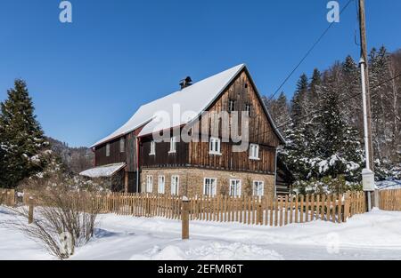 Cottage di legno nel villaggio. Rifugio tipico in inverno in una giornata di sole. Croce di legno di fronte al cottage. Foto Stock