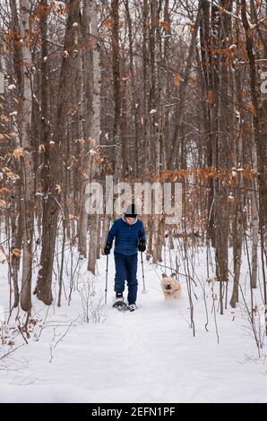 Teen boy racchette da neve con il cane nel bosco in una giornata invernale innevata. Foto Stock