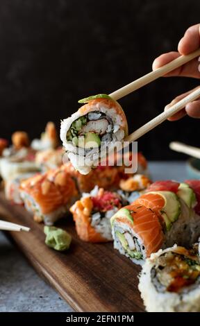 Primo piano di bastoncini che tengono un rotolo di sushi sopra un piatto di cibo. Foto Stock