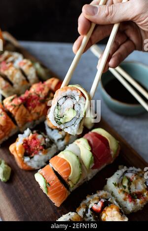 Primo piano del rotolo di sushi che tiene la mano usando le bacchette sopra un piatto. Foto Stock