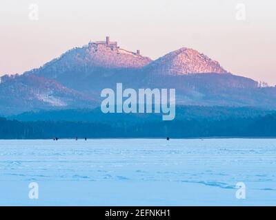 Castello di Bezdez sopra il lago ghiacciato Machovo con pattinaggio su ghiaccio o persone a piedi. Paesaggio invernale, congelare foresta con neve. Luce blu rosa prima del tramonto. Foto Stock