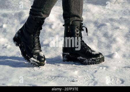 Le gambe della donna in alti stivali neri che camminano lungo la strada nella neve Foto Stock