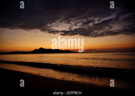Mattina presto, poco prima dell'alba, sulla spiaggia di Alcudia a Maiorca, Spagna. Splendida vista sul mare, montagne all'orizzonte e nuvole scure Foto Stock