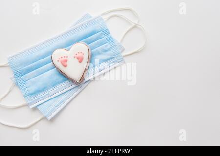 Maschera medica monouso e due cuori. Cuore con footprint del bambino. Parto nella pandemia del coronavirus Foto Stock