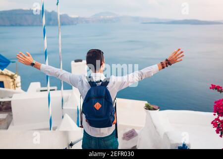 L'uomo viaggiatore dell'isola di Santorini gode della vista della Caldera da Oia, Grecia con le braccia sollevate. Tradizionali case bianche e paesaggio marino. Turismo, viaggiare, Foto Stock