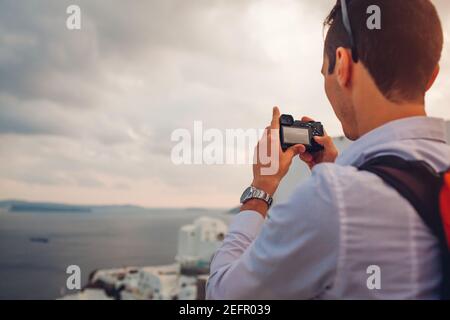 Uomo viaggiatore di Santorini scattare foto della Caldera da Oia, Grecia con la fotocamera. Turismo, viaggi, vacanze estive. Turista che ammira il paesaggio del mare Egeo. Foto Stock