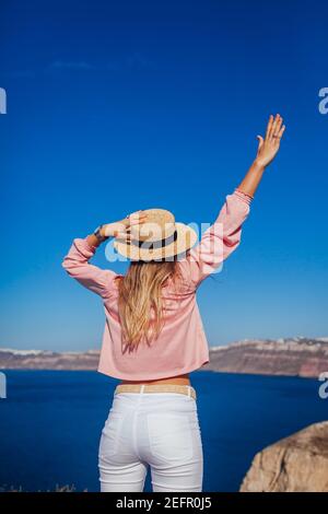 Donna viaggiatore a piedi sull'isola di Santorini, Grecia godendo del paesaggio marino. Happy girl gode di vista Caldera con braccio sollevato. Vacanze estive Foto Stock