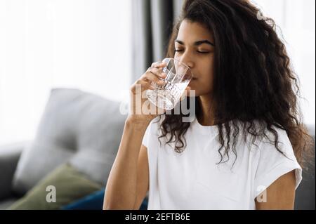 Bella ragazza seguire uno stile di vita sano, bere un'acqua pura. Donna afroamericana bere quantità giornaliera di acqua pulita, sano stile di vita concetto Foto Stock