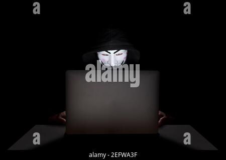 Membro del gruppo di hacker anonimi che indossa una maschera davanti al suo laptop mentre commette un hack. Foto Stock