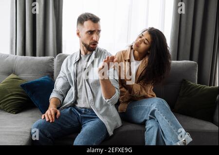 Sorridente nero multirazziale riccia ragazza usa il telefono cellulare, parlando con gli amici o la famiglia mentre si siede sul divano in soggiorno e guarda la macchina fotografica, concetto di comunicazione Foto Stock