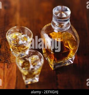 Una bottiglia di whisky e due bicchieri di Scotch sul Rocce su un tavolo di legno Foto Stock
