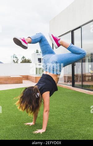 Ragazza adolescente con capelli lunghi che indossa abiti casual facendo acrobazie, in piedi su una terrazza o spazio all'aperto Foto Stock