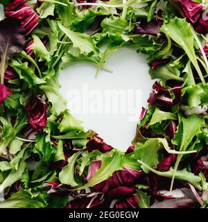 Forma del cuore da foglie di insalata verde e viola mescolano lo sfondo. Tavola bianca. Foto di alta qualità Foto Stock