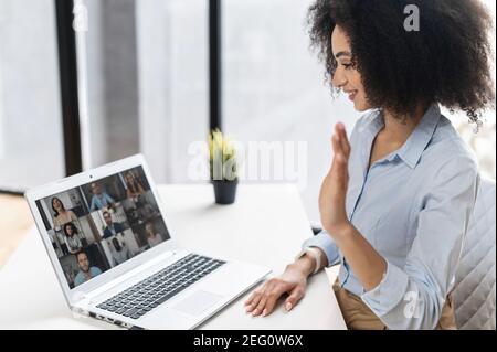 Donna di razza mista seduta in ufficio e che utilizza un'applicazione per la comunicazione video a distanza con colleghi, partecipanti al webinar, incontro online Foto Stock