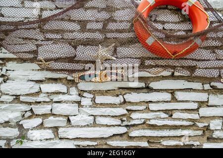 Muro di mattoni bianchi decorato con reti da pesca, pesci ornamentali, stelle marine e boa vita arancio in un ristorante di pesce. Foto Stock