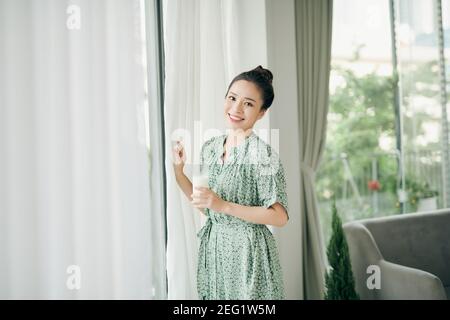 Una giovane donna che beve latte a casa vicino alla finestra, cibo sano. Foto Stock