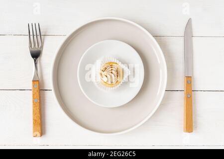 Concetto di alimentazione e dieta sana. Piccolo dessert su un piatto grande servito con forchetta e coltello su tavola bianca. Foto Stock