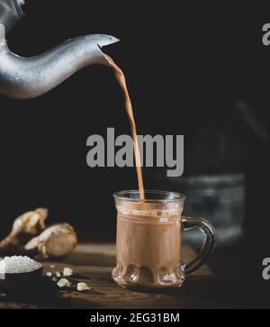 Versare il tè nella tazza di vetro - concetto di ingredienti masala richiesto per la preparazione del tè con aspetto vintage. Foto Stock