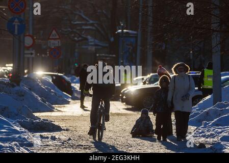 RIGA, LETTONIA. 12 febbraio 2021. Foto con messa a fuoco selettiva. Un uomo corre in bicicletta. Passeggiate in famiglia con slitta. Foto Stock