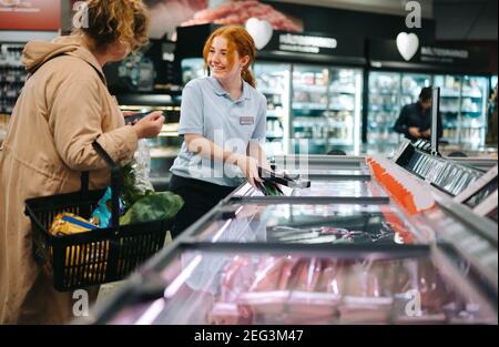 Donna che lavora in un supermercato assistendo un cliente. Dipendente del negozio di alimentari che aiuta una donna acquirente. Foto Stock