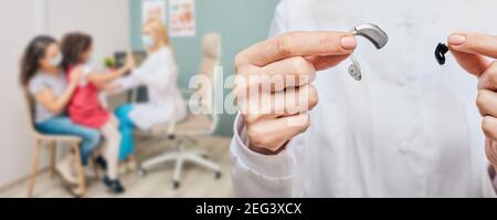 Dietro l'orecchio e gli apparecchi acustici intrauricolari nelle mani dei medici, primo piano. Selezione di apparecchi acustici per pazienti pediatrici sullo sfondo Foto Stock