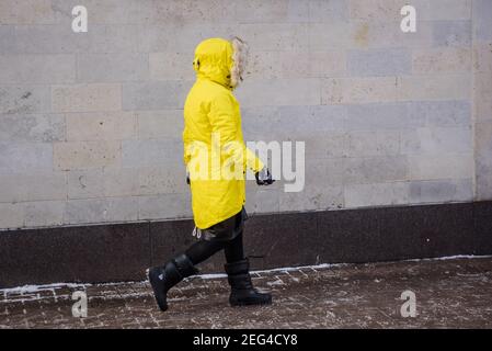 RIGA, LETTONIA. 12 febbraio 2021. Donna che indossa abiti caldi cammina sulla strada. Freddo giorno d'inverno. Foto Stock