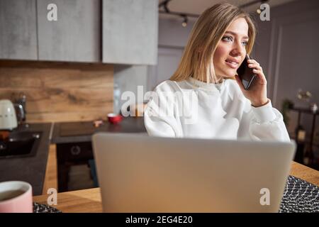Donna che parla sullo smartphone vicino al computer portatile Foto Stock
