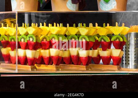 Pezzi di frutta esotica su bastoni, fragole, pere, kiwi e ananas. Visualizzazione precisa in una custodia in vetro trasparente. Foto Stock