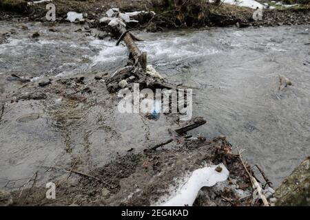 Bottiglia di plastica su un ruscello di montagna durante una fredda e soleggiata giornata invernale nei Monti Carpazi rumeni. Foto Stock