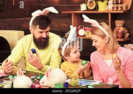 Padre, madre e figlio dipingendo le uova di Pasqua. Famiglia felice con orecchie conigliate. Foto Stock