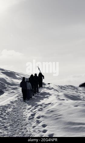 Gli sciatori e gli snowboarder con sci e snowboard saliscono su una strada innevata al mattino presto d'inverno. Montagne del Caucaso, Georgia, regione Gudauri. Nero e w Foto Stock