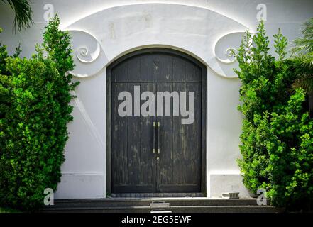 Una grande entrata a doppia porta ad un lussuoso complesso di proprieta', con un contorno di intonaco bianco ad arco, incorniciato da lussureggiante arbustia verde. Foto Stock