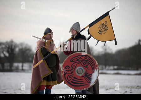 Vikiing Shield Maiden, con raven zitto e bandiera, in piedi in amicizia con il guerriero anglosassone in un paesaggio ghiacciato. Foto Stock