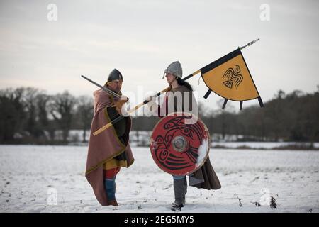 Vikiing Shield Maiden, con raven zitto e bandiera, in piedi in amicizia con il guerriero anglosassone in un paesaggio ghiacciato. Foto Stock