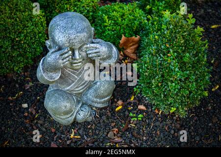 Statua di monaco buddista in pietra in un giardino usando l'azione della mano per chiudere gli occhi. Concetto di scimmia tre Foto Stock