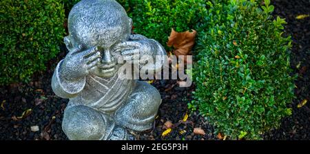 Statua di monaco buddista in pietra in un giardino usando l'azione della mano per chiudere gli occhi. Concetto di scimmia tre Foto Stock