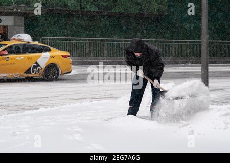 Mosca. Russia. 12 febbraio 2021. Un operatore di servizi che indossa una maschera protettiva, indossa una pala per la neve su una strada cittadina durante una nevicata su un Foto Stock