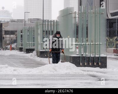 Mosca. Russia. 12 febbraio 2021. Un operatore che indossa una maschera protettiva rimuove la neve con uno scraper su una strada cittadina durante una nevicata su un Foto Stock