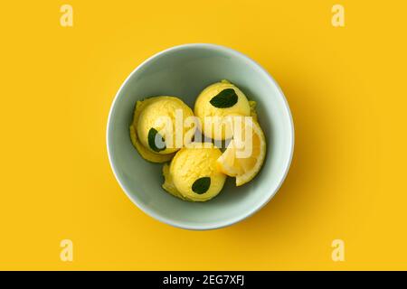 Paletta per gelato al limone decorata con foglie di menta in una ciotola su sfondo giallo Foto Stock