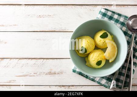 Paletta per gelato al limone decorata con foglie di menta in una ciotola su tavolo di legno Foto Stock