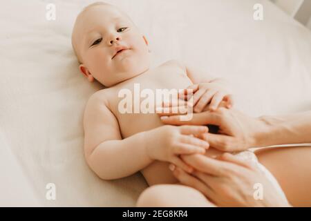 Massaggio del bambino, mamma massaggia il ventre del bambino durante colica, neonato con colica sdraiata sulla schiena senza vestiti, la mano della madre sul suo stomaco lo aiuta Foto Stock