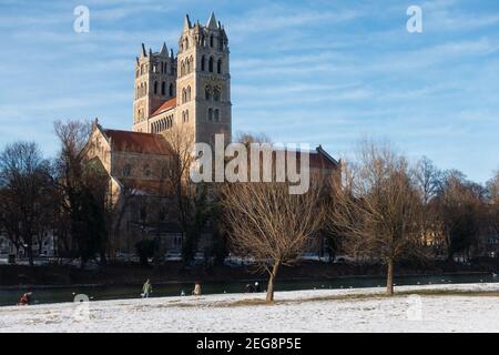 Vista dal fiume Isar sulla chiesa parrocchiale di San Massimiliano, nella soleggiata giornata invernale. Ci sono alcune persone che camminano al fiume Foto Stock