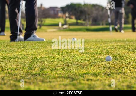 Colpo d'ora d'oro del campo da golf con il fuoco su una sfera sul campo. Le gambe dei golfers possono anche essere viste sul lato. Foto Stock