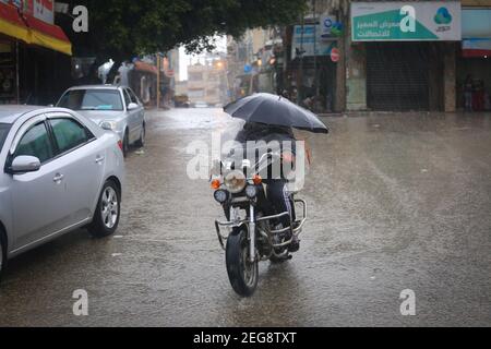 Gaza, Palestina. 18 Feb 2021. Un uomo palestinese ride moto uso ombrello come pioggia cade a Gaza City, il 18 febbraio 2021. (Foto di Mahmoud Khattab/INA Photo Agency/Sipa USA) Credit: Sipa USA/Alamy Live News Foto Stock