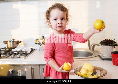 Adorabile bambina che aiuta e cuoce la torta di mele nella cucina interna della casa Foto Stock